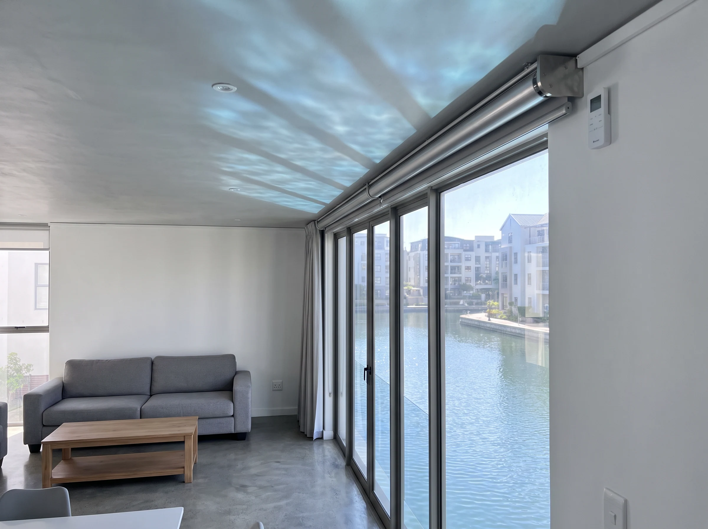 Motorised roller blind tube mechanism with a wall-mounted remote control beside a Century City apartment window